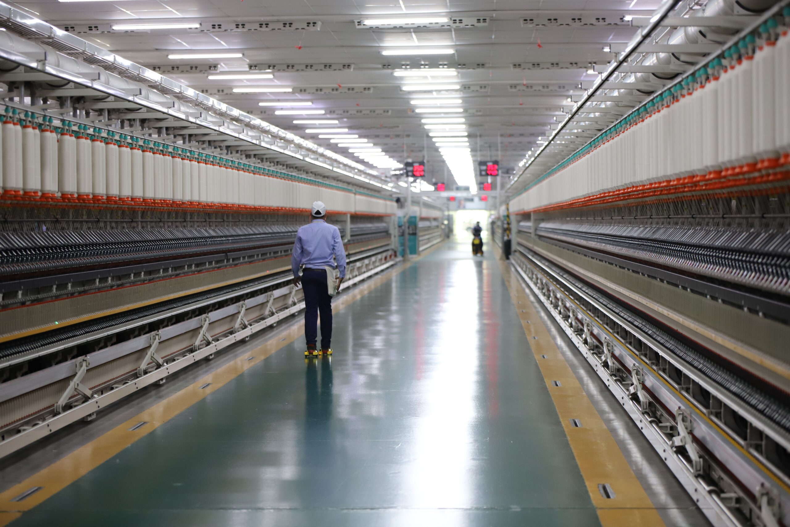 A worker walks through a wide hallway in an industrial textile plant, India.